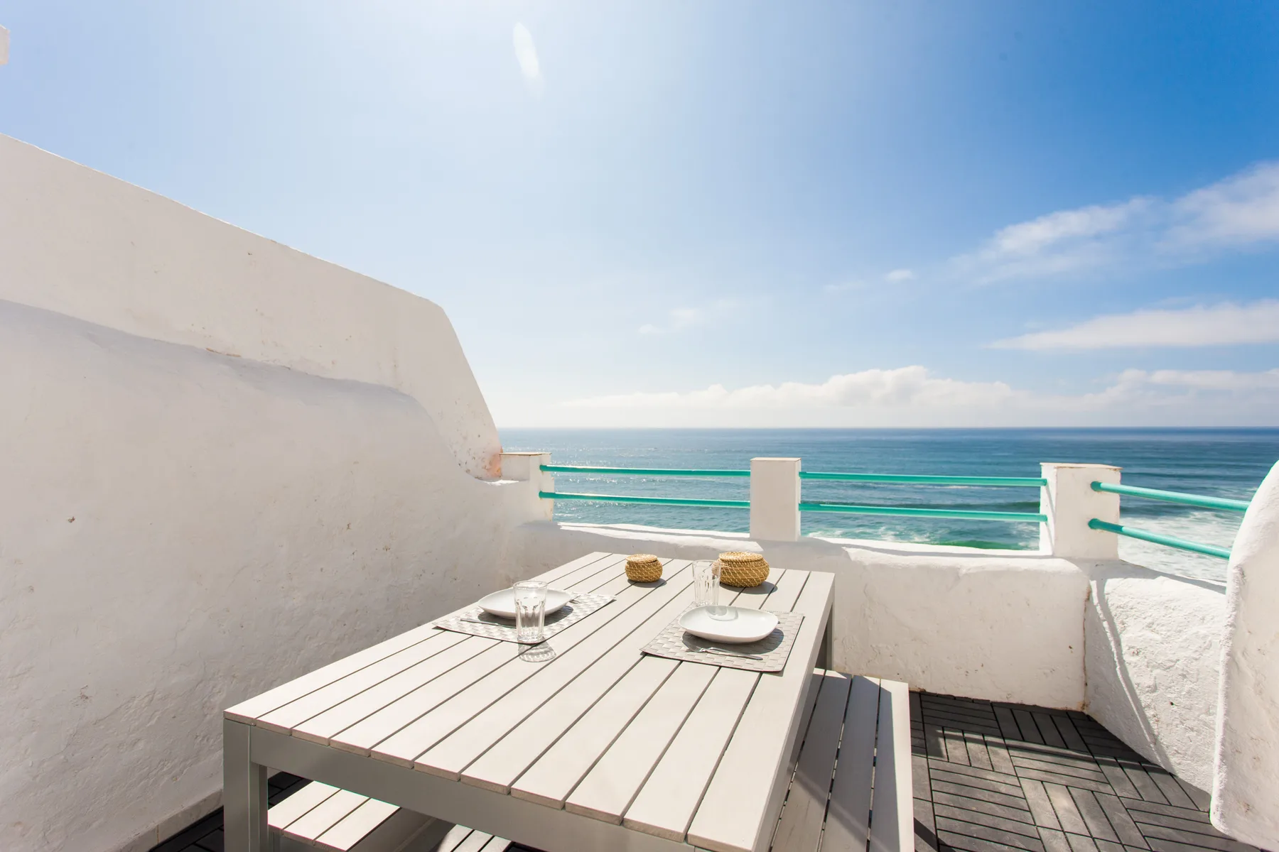 A seaside terrace has a dining table overlooking the ocean.