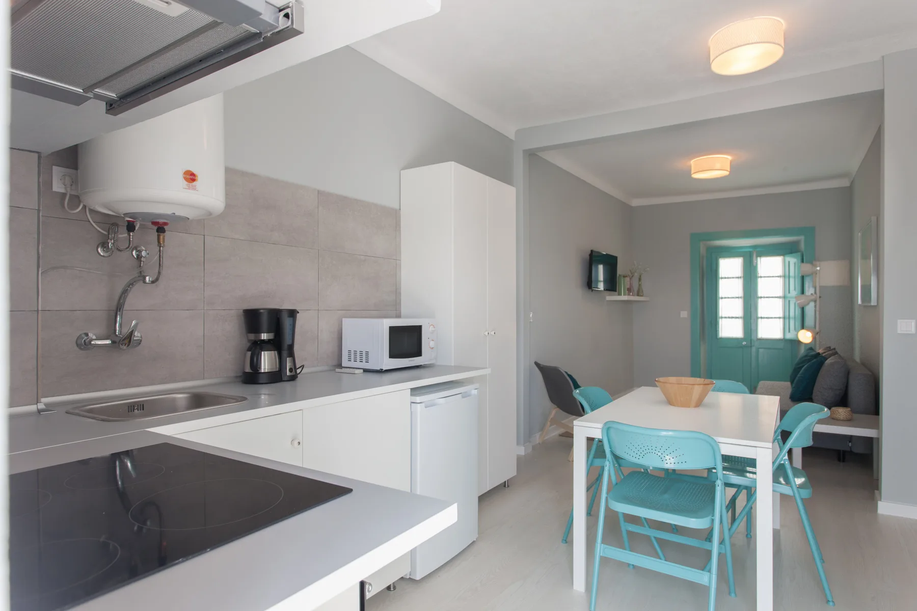 A compact kitchen and dining area with white cabinetry and turquoise seating.