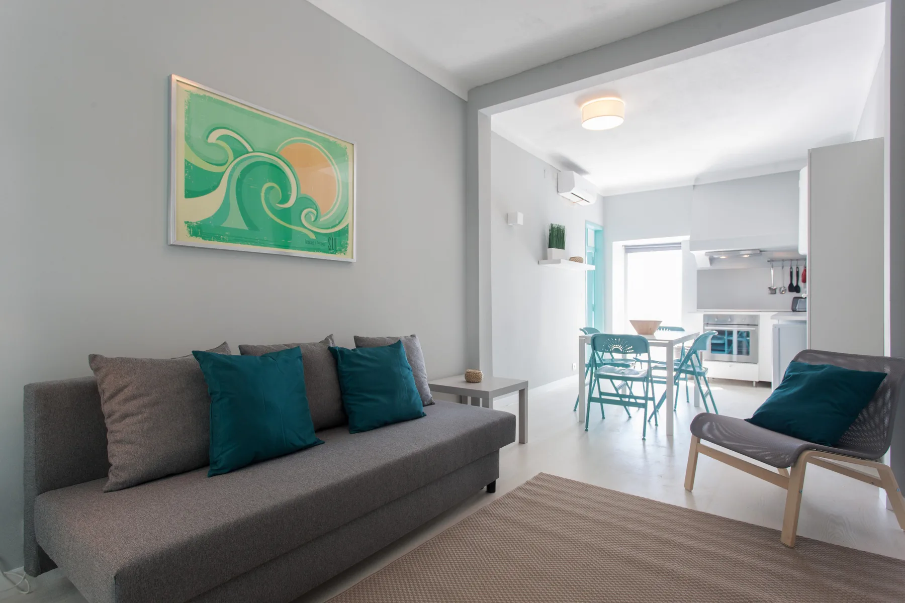 A living room with a sofa, teal cushions, and a dining area beyond.