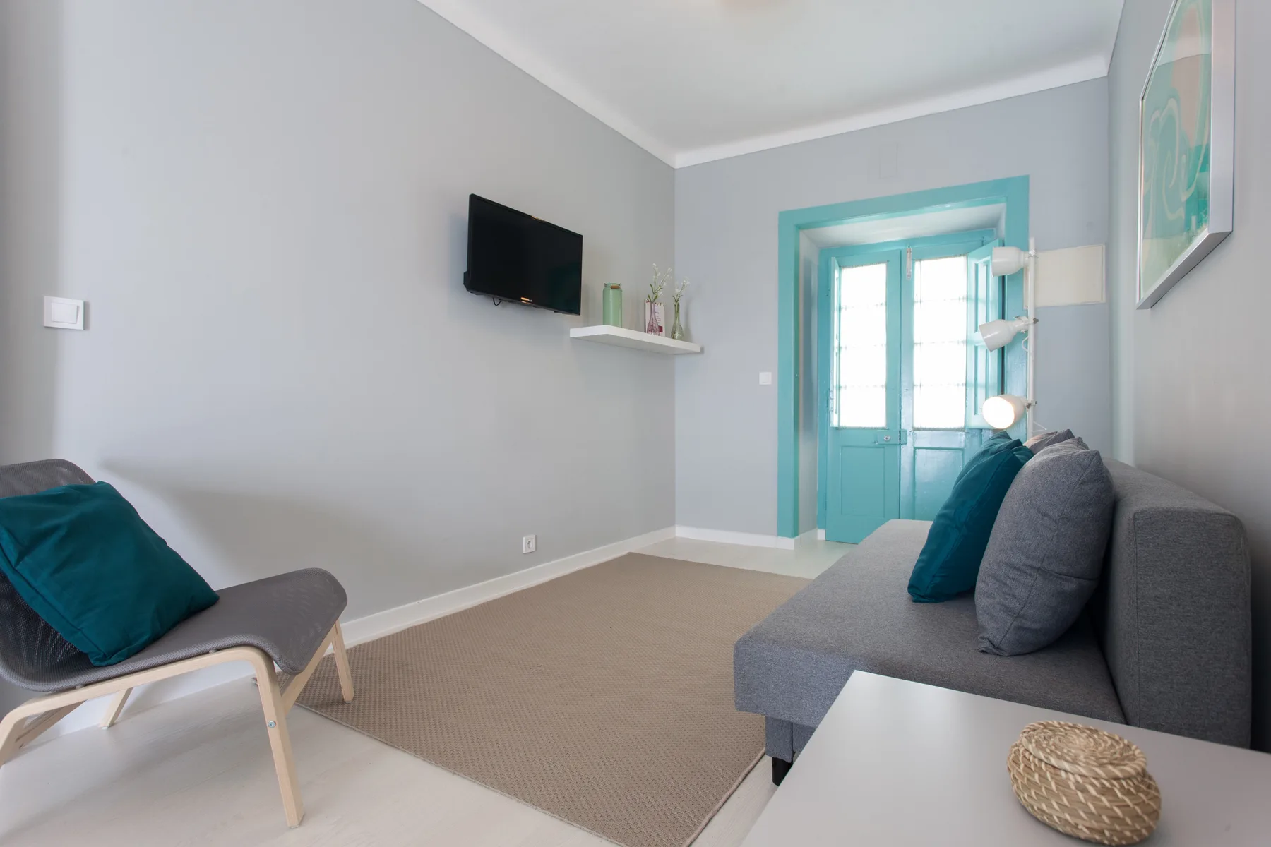A living room with seating, a wall-mounted television, and a turquoise doorway.