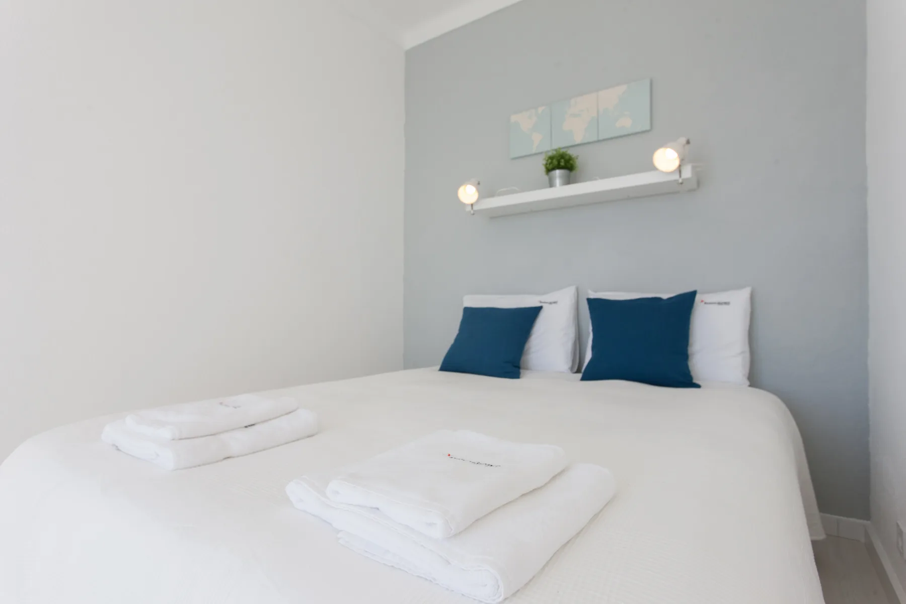 A bedroom with a neatly made bed, folded towels, and blue accent pillows.