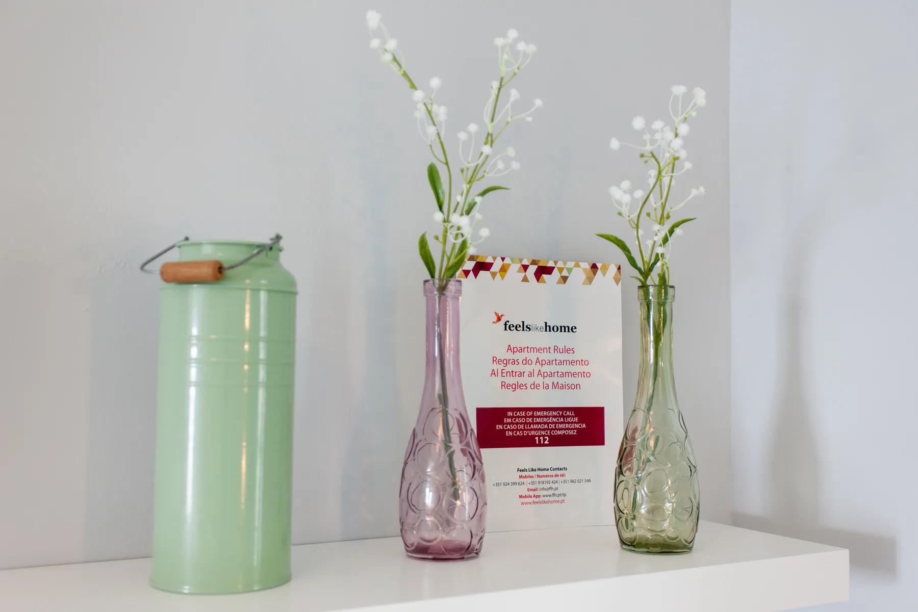 A shelf displays a green container, two flower vases, and a printed card.