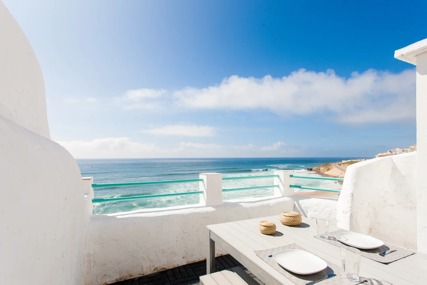 A seaside terrace overlooks the ocean, with a white outdoor table and seating.