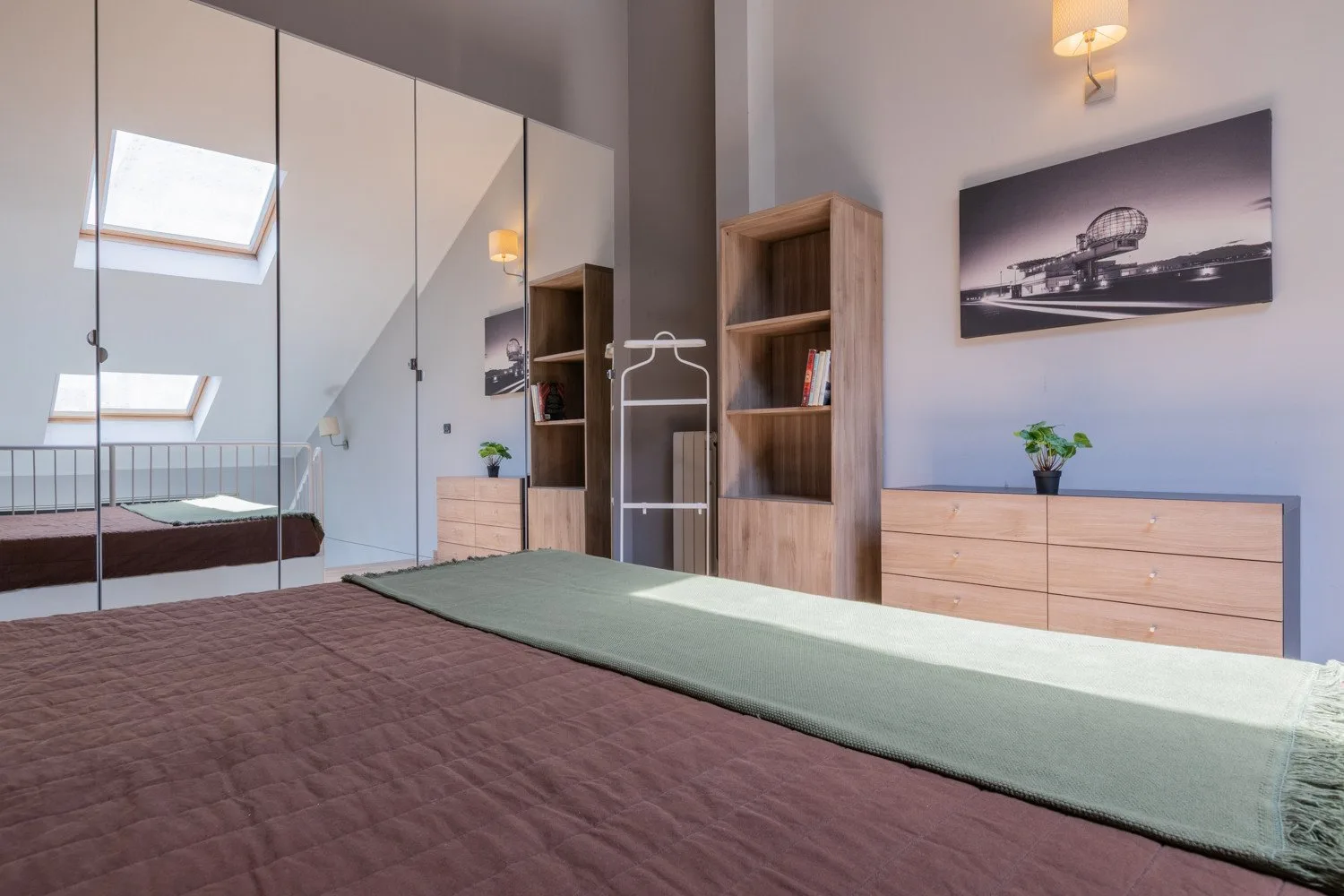 Un dormitorio con una cama, un armario con espejo y muebles de almacenaje de madera.