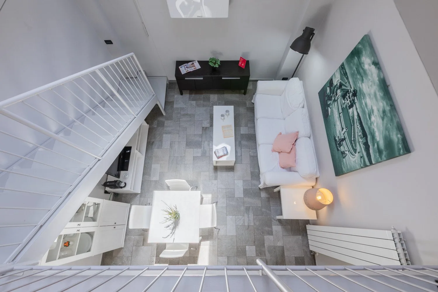 Sala de estar tipo loft con sofá blanco, mesa de centro y suelo de baldosas grises.
