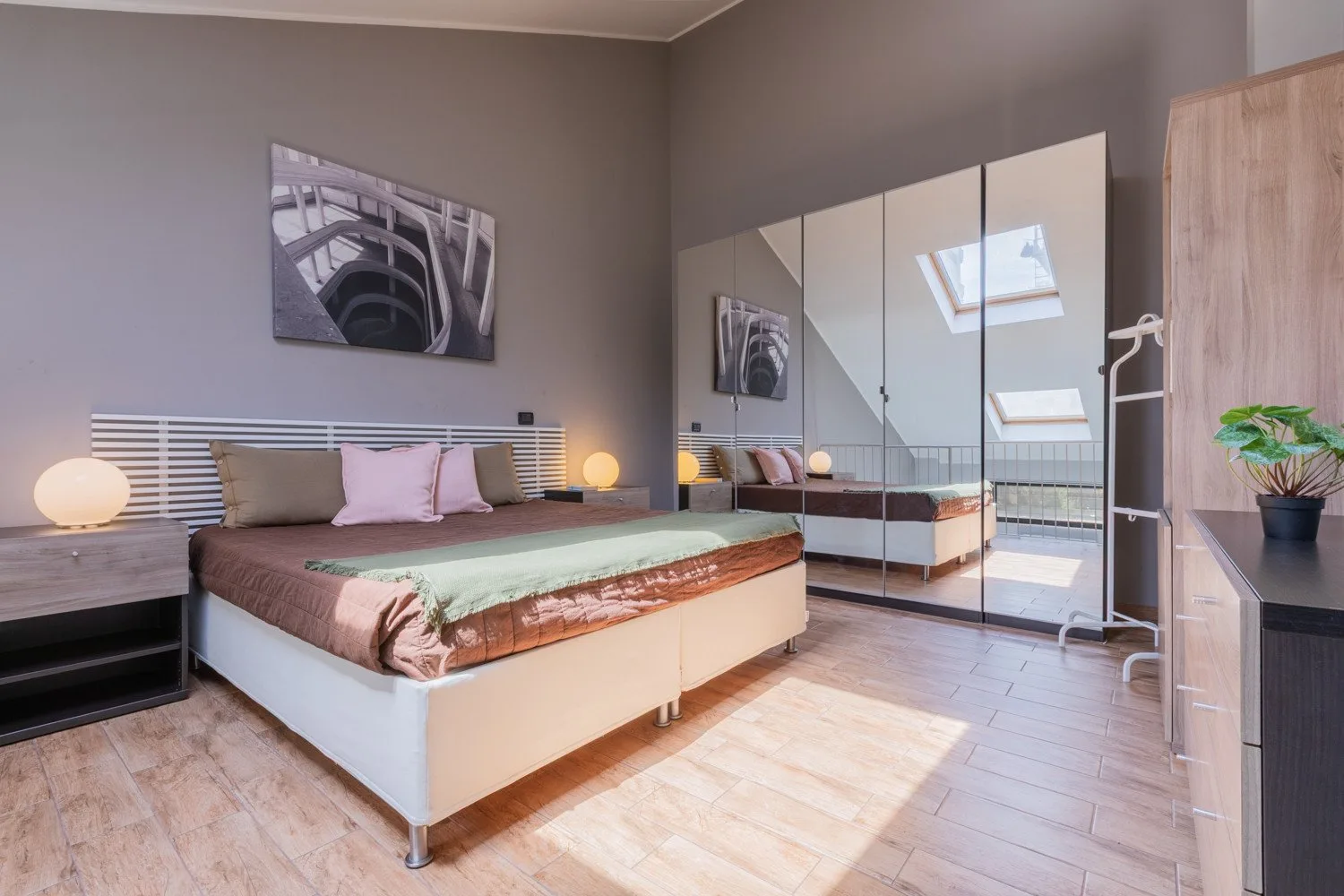 Un dormitorio con una cama baja, un armario con espejo y lámparas de noche.