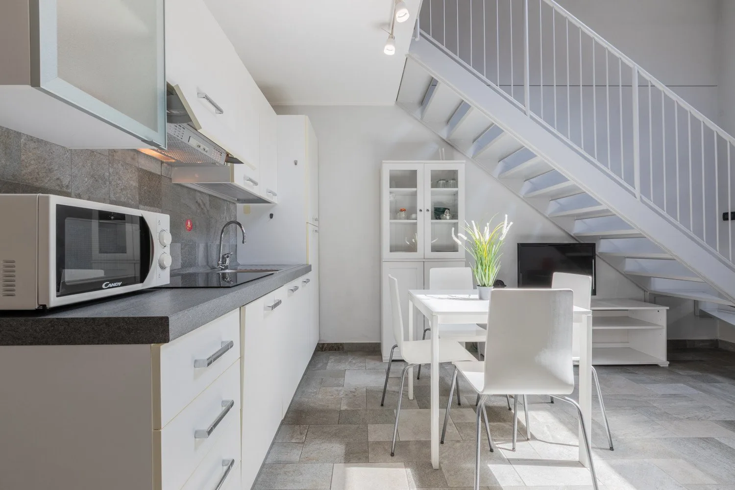 A bright open-plan kitchen and dining area with a table beneath a staircase.