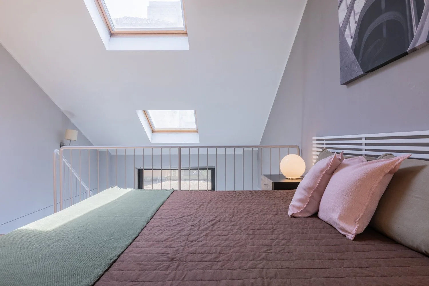 Un dormitorio abuhardillado con una cama bajo un techo inclinado y tragaluces.