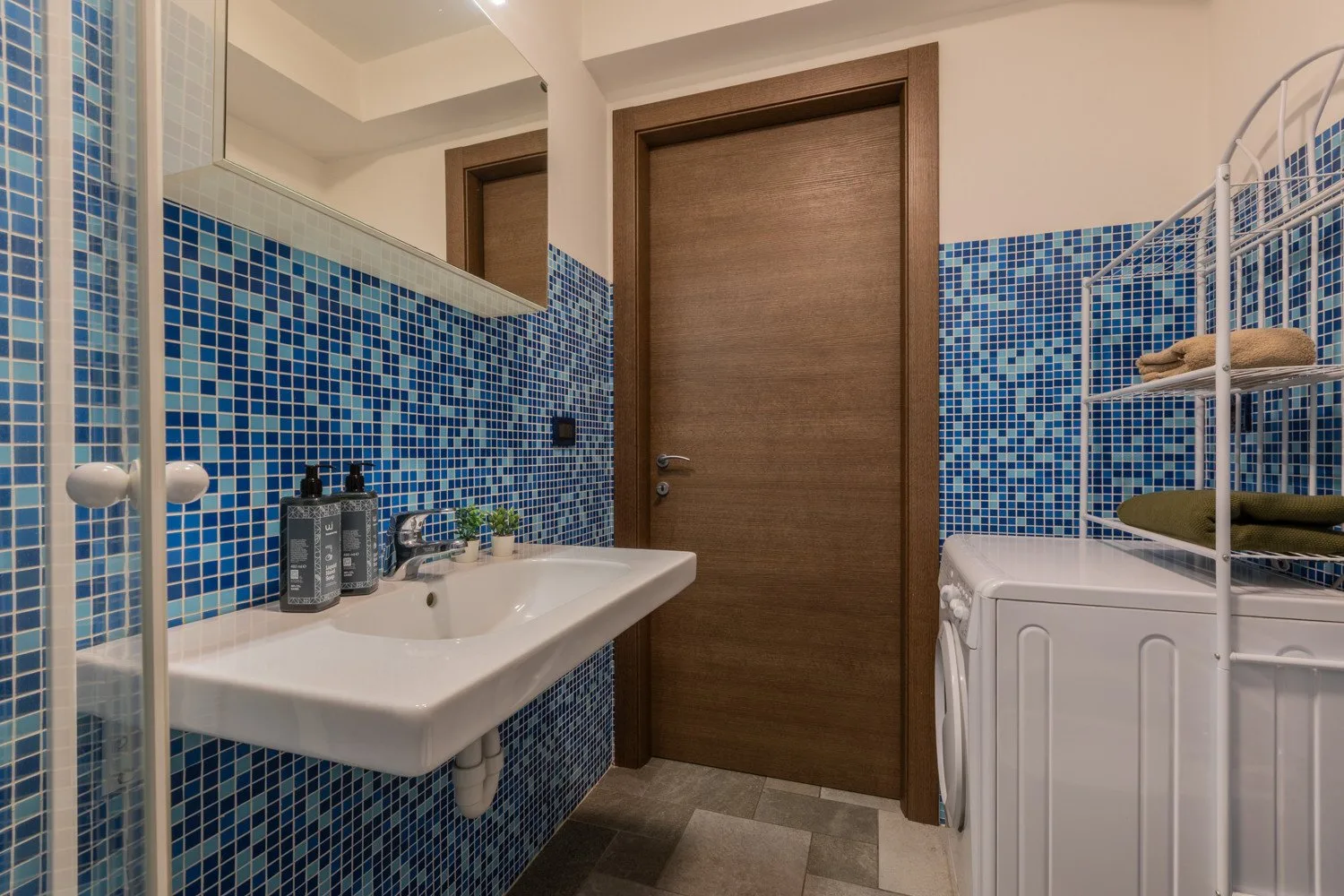 Un baño con un lavabo blanco, paredes de azulejos azules y una puerta de madera.