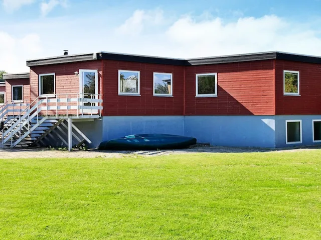 Una casa roja está junto a un césped verde, con una pequeña embarcación junto a la pared.