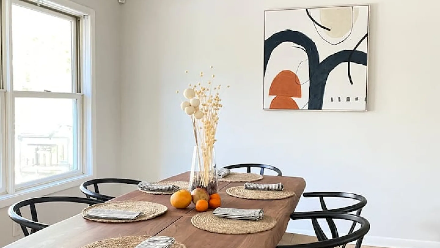 A dining area with a wooden table set with placemats and dried flowers.