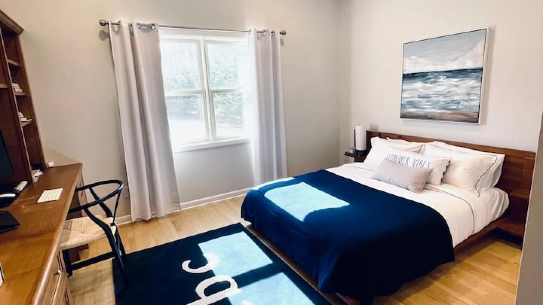 Un dormitorio con una cama cubierta con una manta azul oscuro junto a una ventana con cortinas.