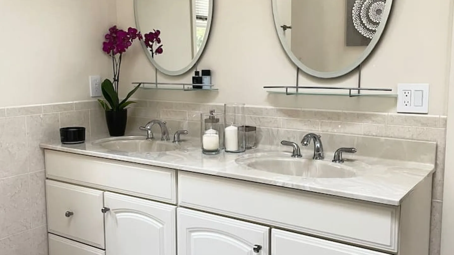 Un tocador de baño tiene dos lavabos, espejos y una planta con flores sobre la encimera.