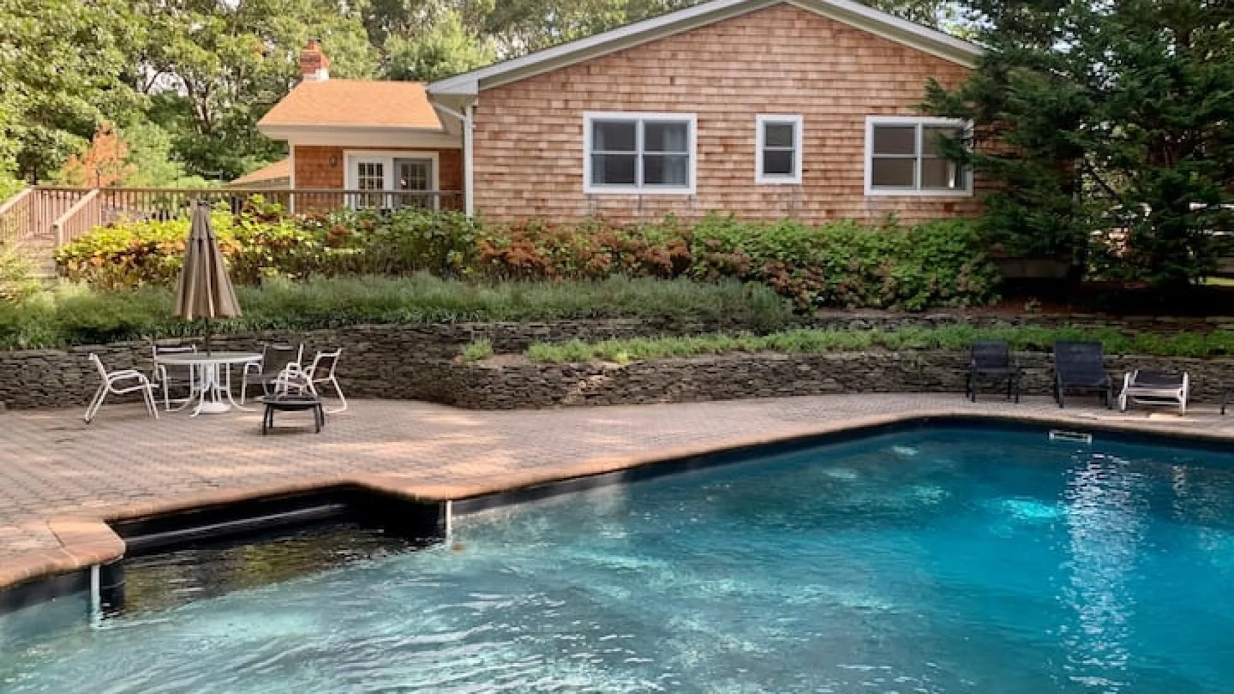 Una piscina al aire libre y un patio pavimentado están frente a una casa.