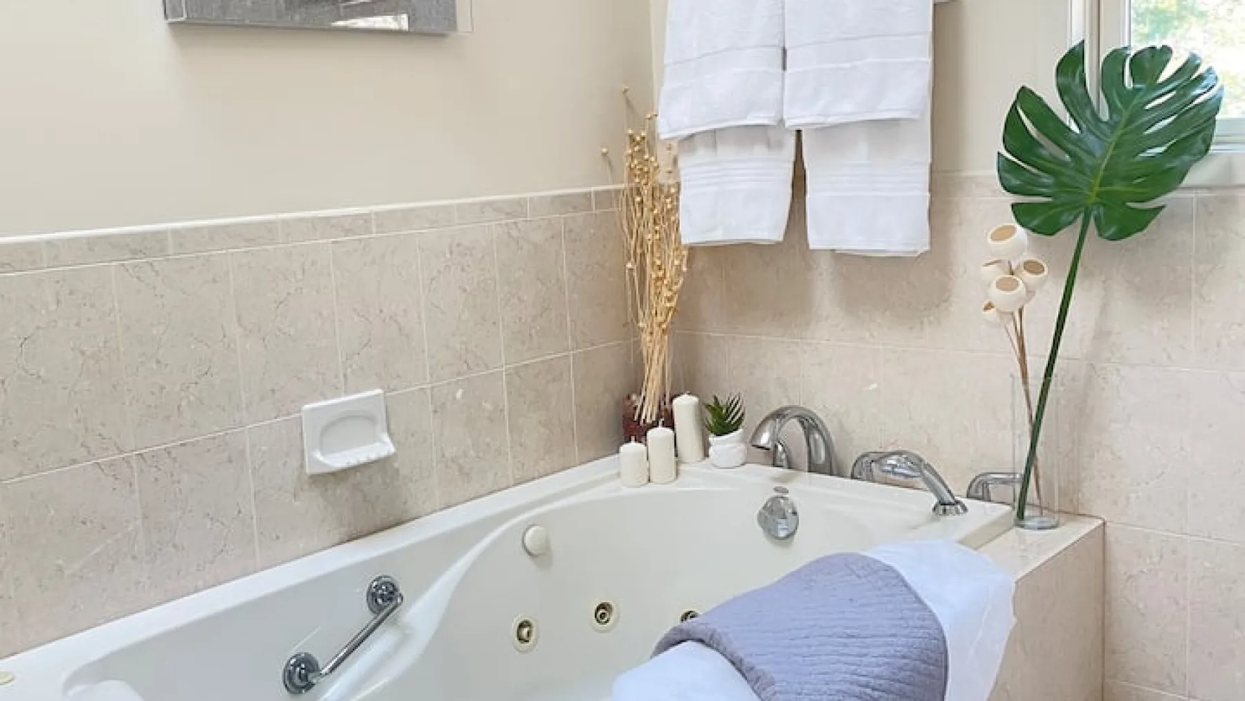 Un baño con una bañera empotrada, toallas dobladas y una planta de hojas grandes.