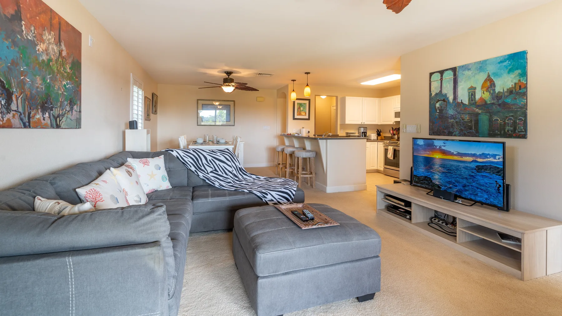 A living room with gray seating, a television, and an open kitchen.