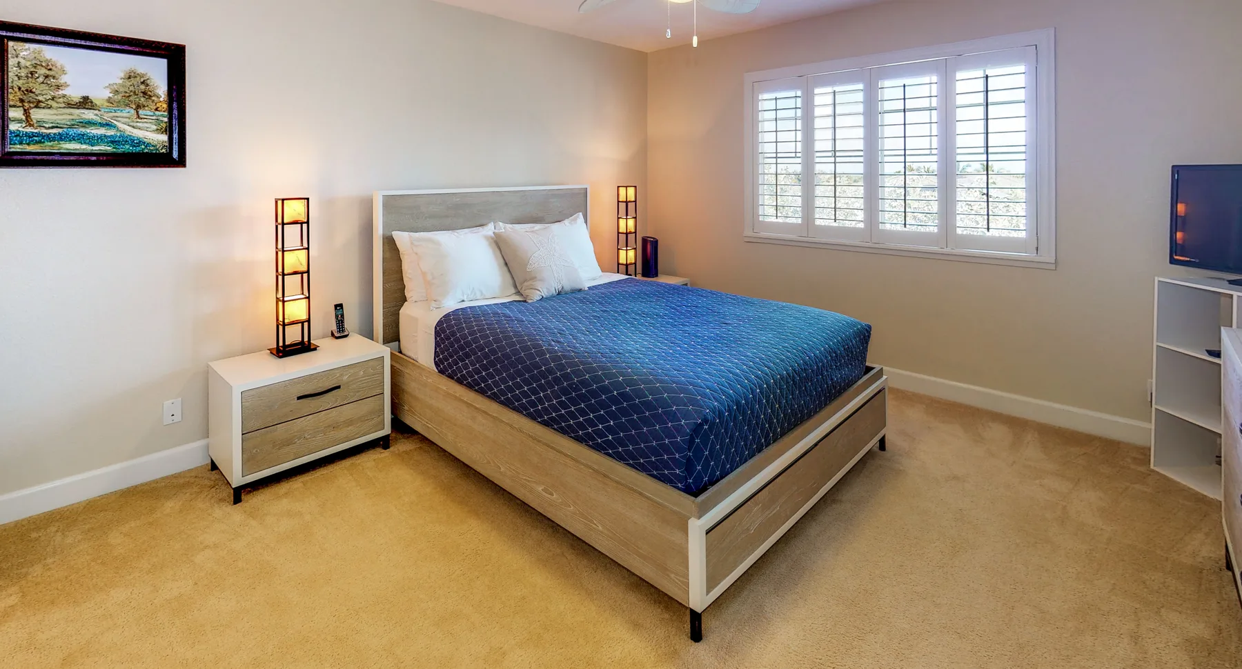 A bedroom with a bed dressed in blue bedding and windows with shutters.