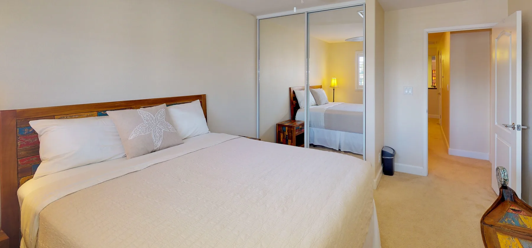 A bedroom with a neatly made bed and mirrored closet doors.