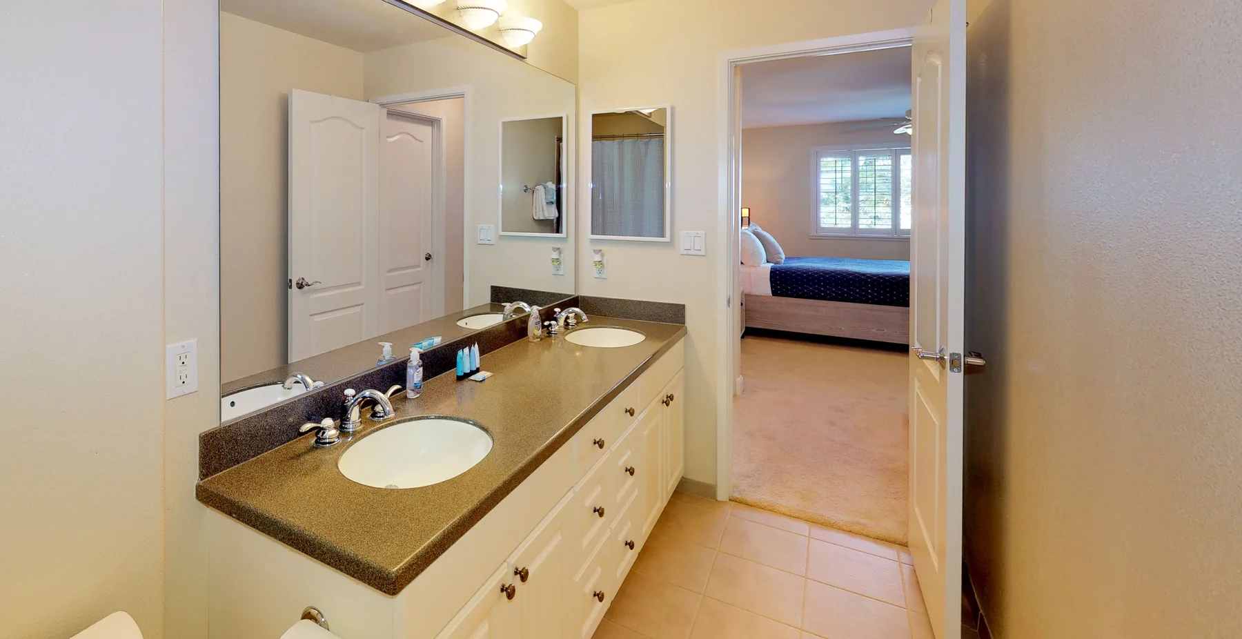 A bathroom vanity with two sinks and a doorway into a bedroom.
