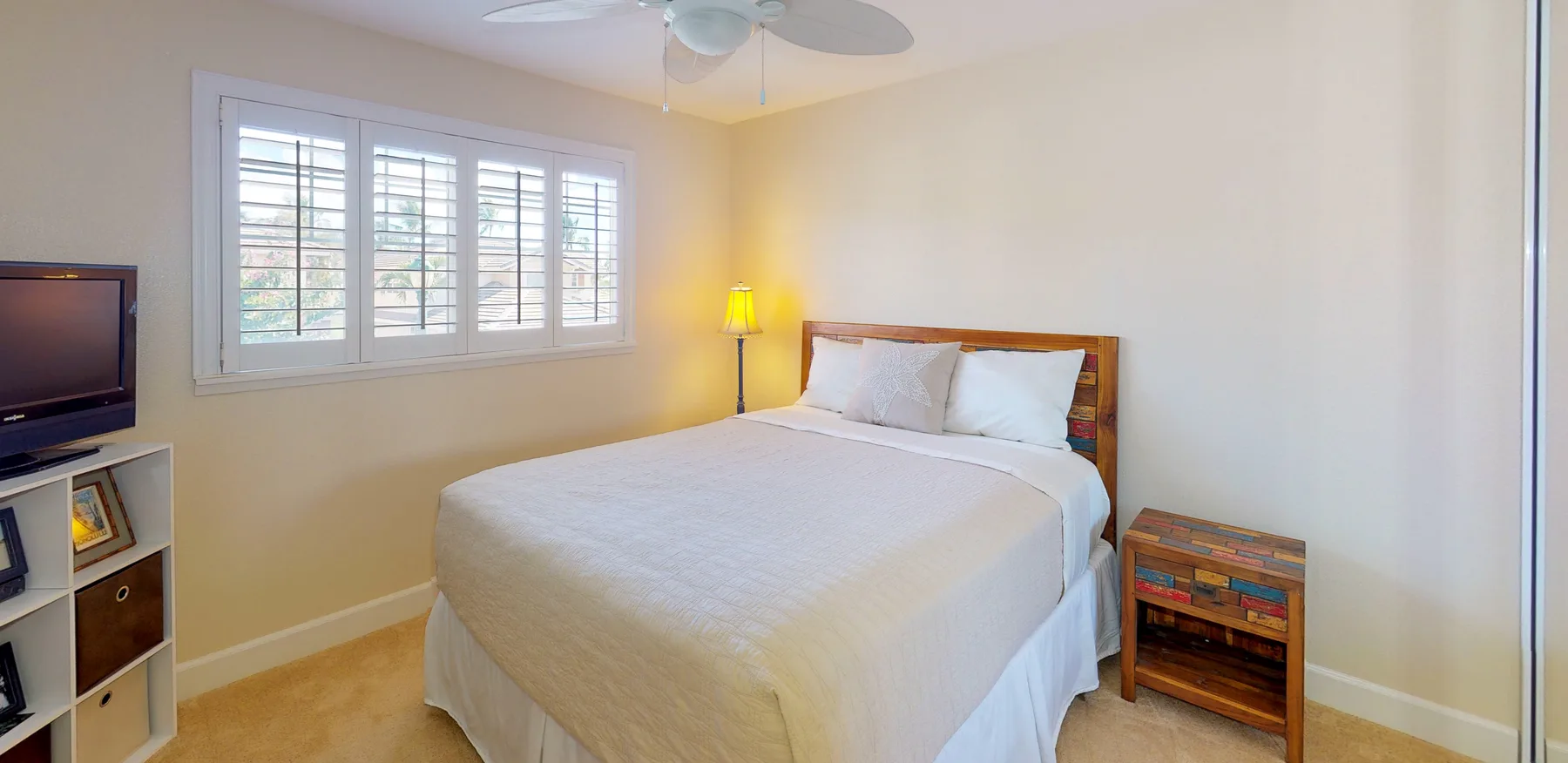 A bedroom with a neatly made bed and windows with white shutters.