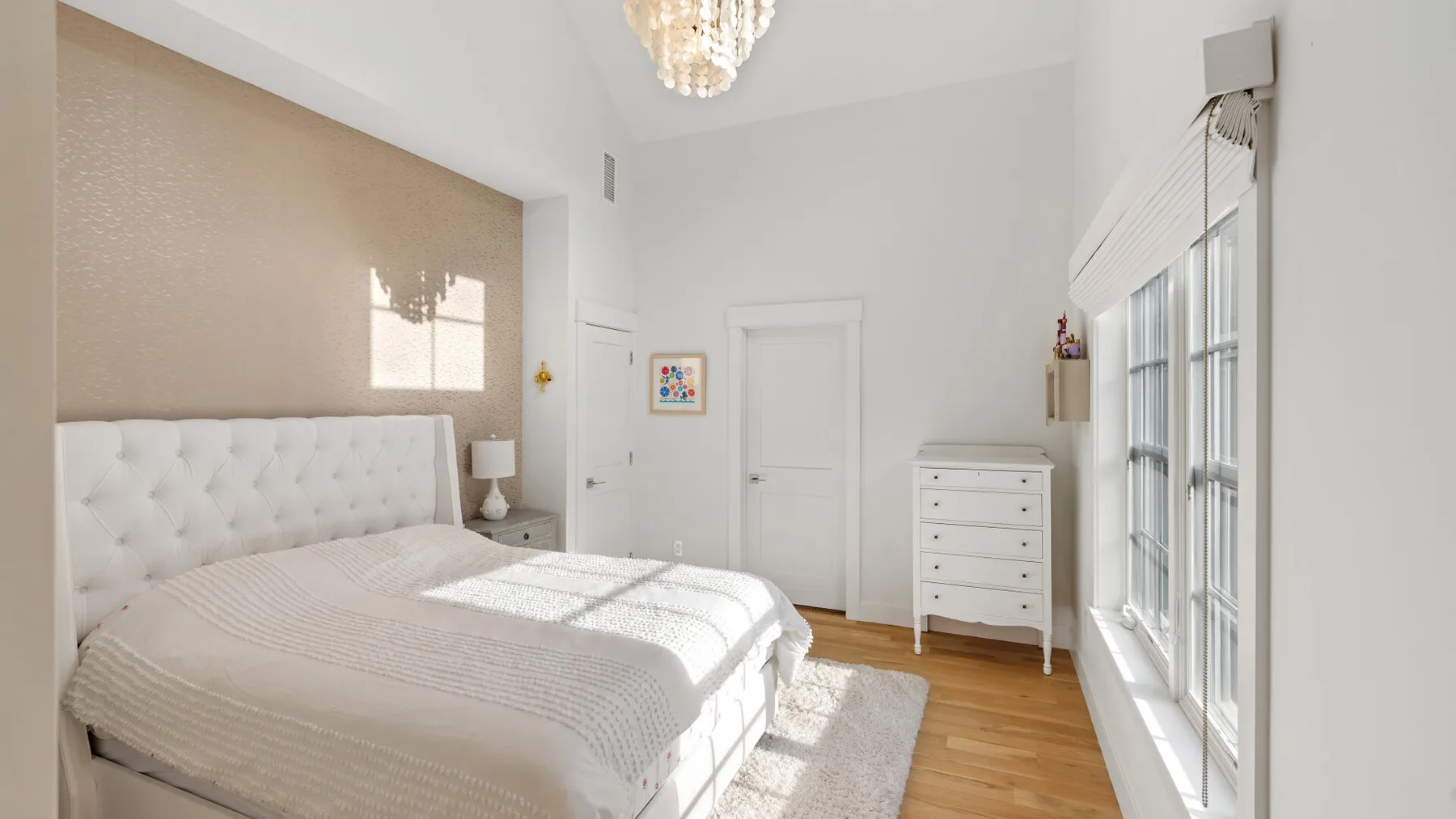 Un dormitorio luminoso con una cama bien hecha y ventanas altas.