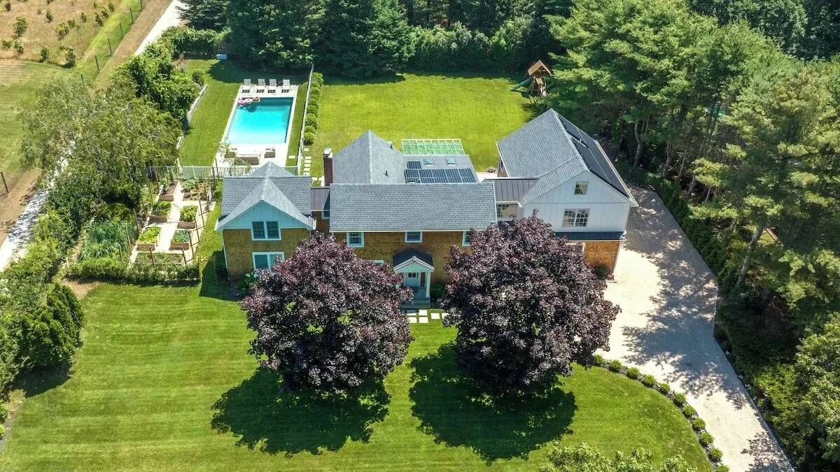 Aerial view of a house surrounded by lawns and trees, with a swimming pool nearby.