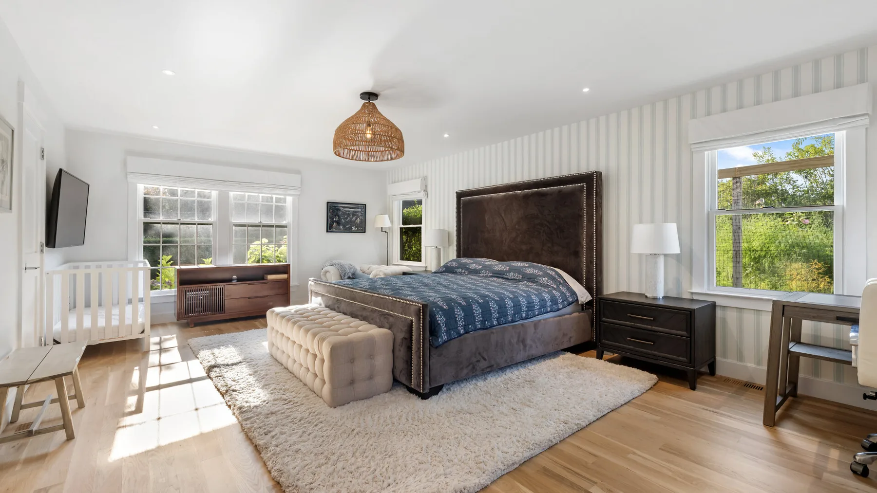 Un dormitorio luminoso con una cama grande, ventanas y suelo de madera clara.