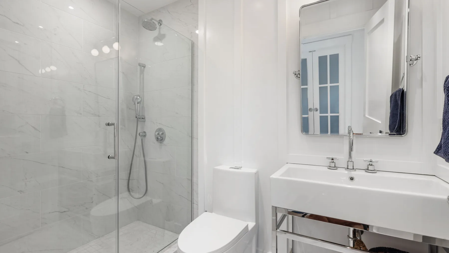 Un baño luminoso con ducha de vidrio, inodoro y lavabo.