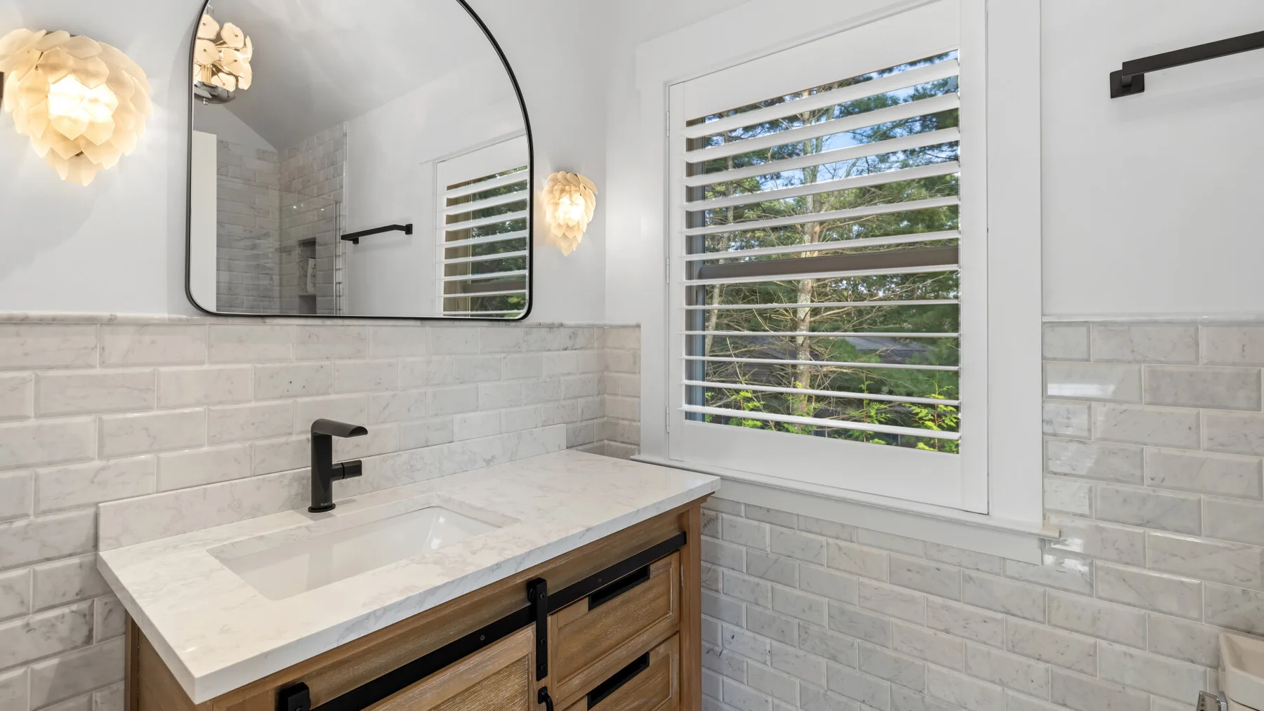 Un lavabo de baño con espejo está junto a una ventana con persianas.