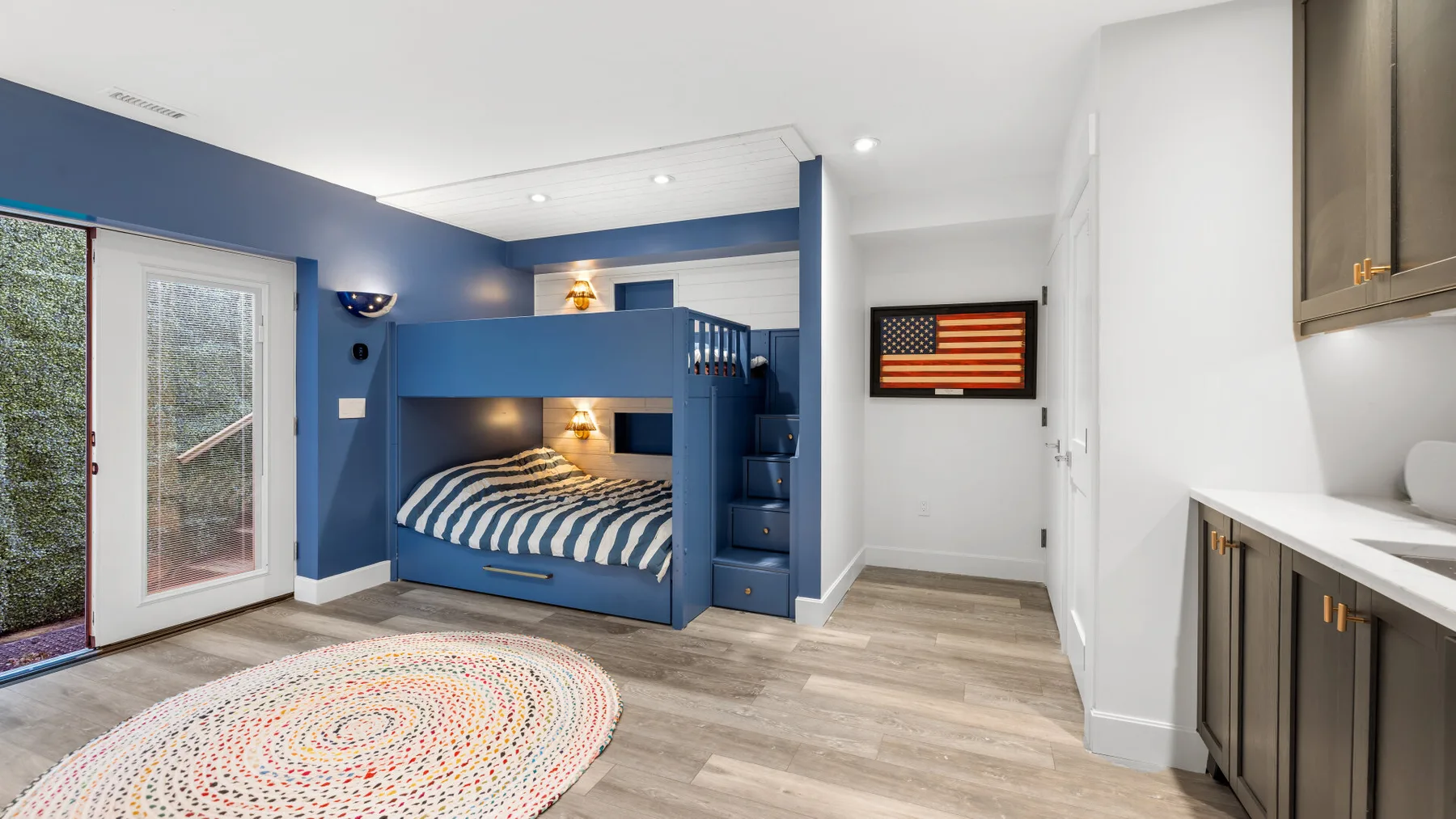 Un dormitorio con literas azules, una alfombra estampada y una pequeña cocina.