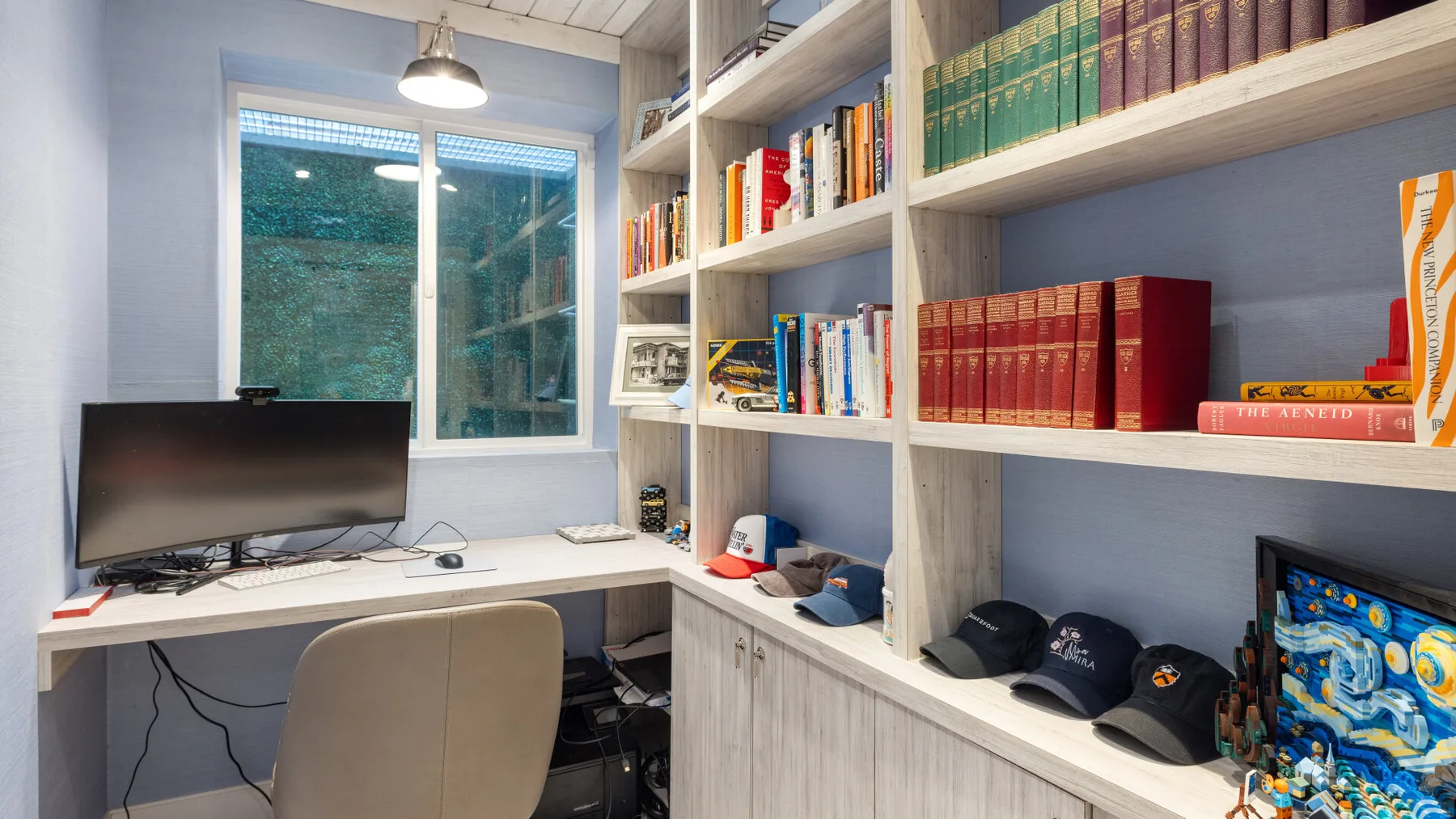 Una pequeña zona de estudio tiene un escritorio, una computadora y estantes con libros.