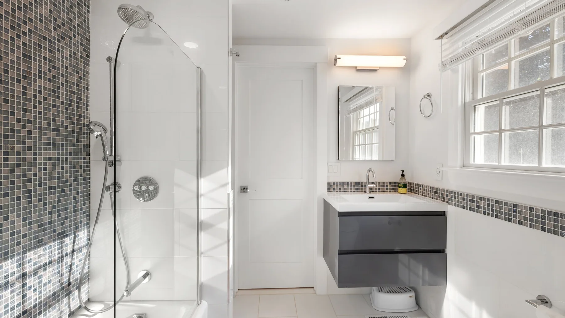 Un baño luminoso con ducha de vidrio, tocador y ventanas grandes.