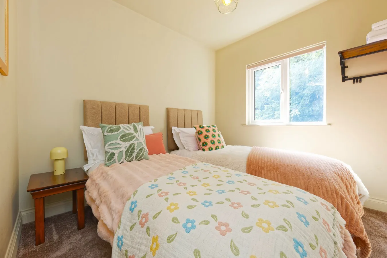 Bedroom with two beds dressed in colorful floral bedding beside a bright window.
