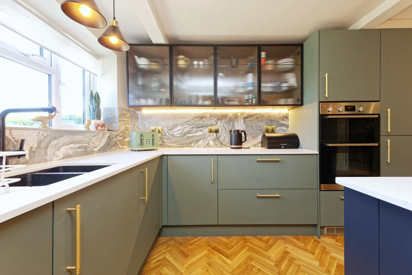 A modern kitchen with green cabinets, a countertop, and a large window.