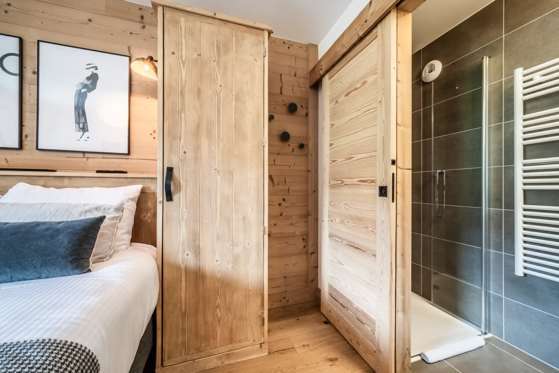 A bedroom with a bed and wood-paneled walls beside a glass shower.