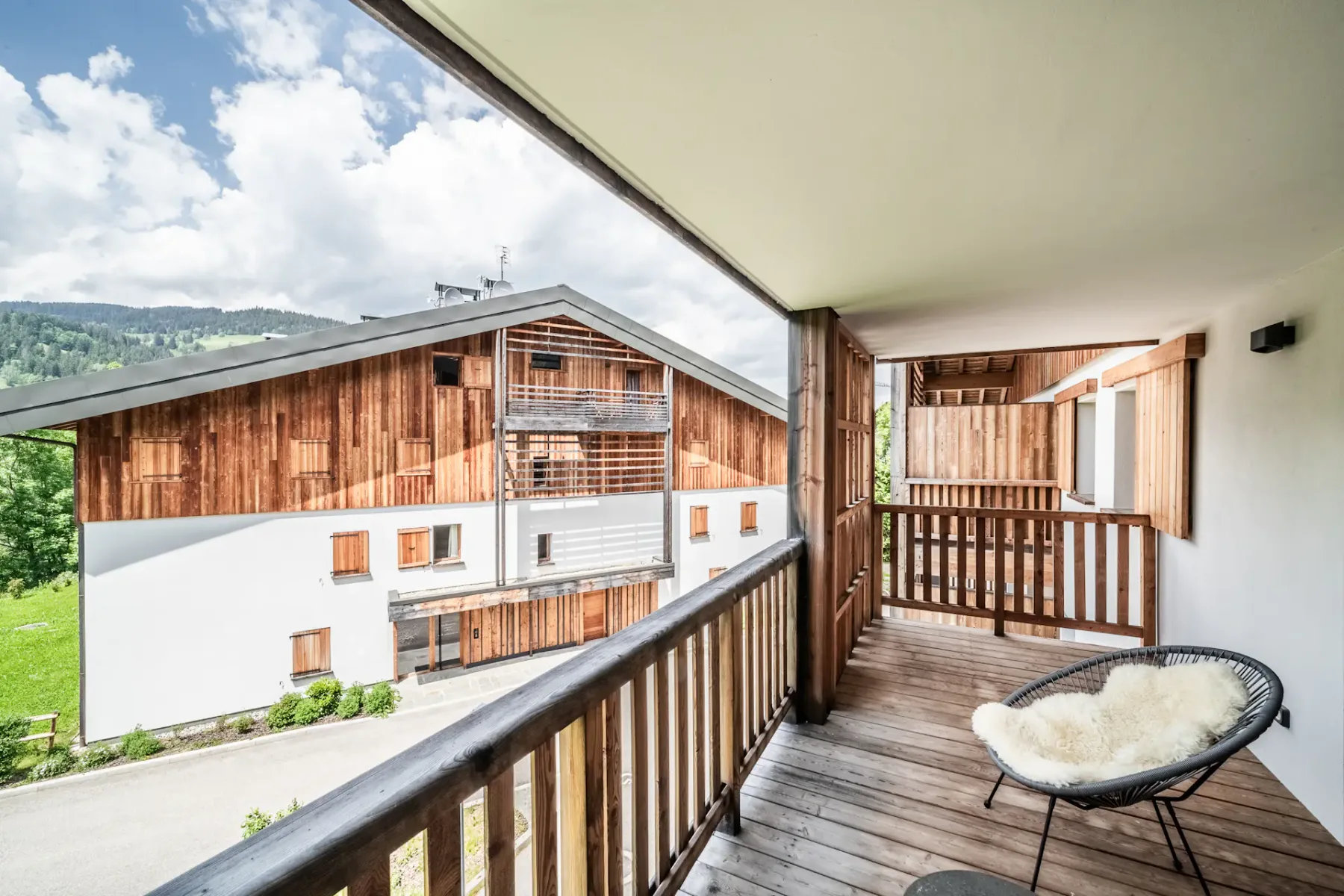 A cozy wooden terrace with a modern chair and table, overlooking green hills, framed by open sliding doors.