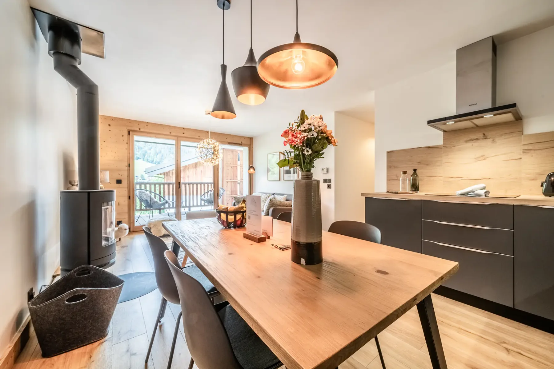 A modern kitchen and dining area with a wooden table, dark seating, and pendant lights.