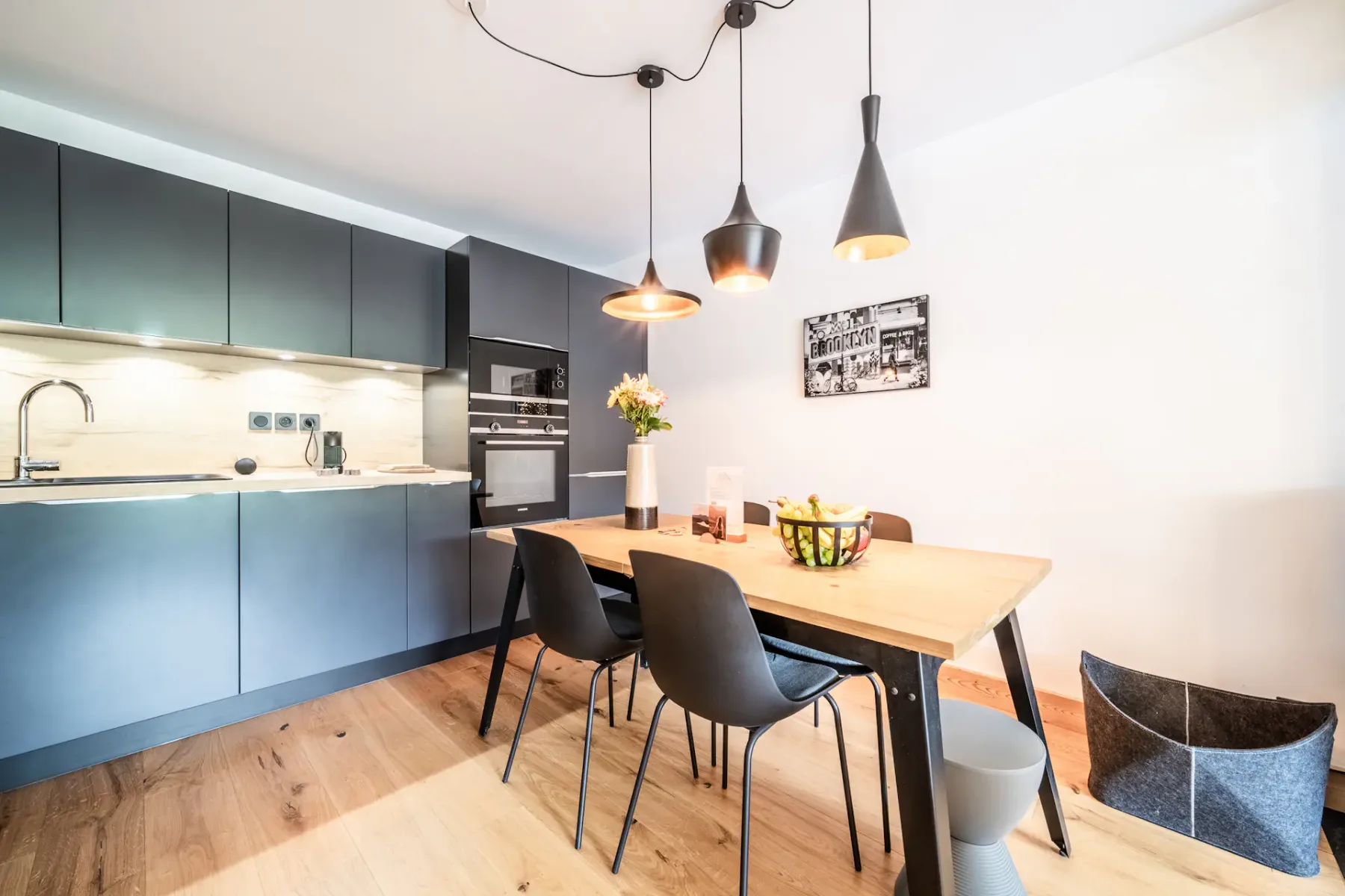 A modern kitchen and dining area with dark cabinets and pendant lights.