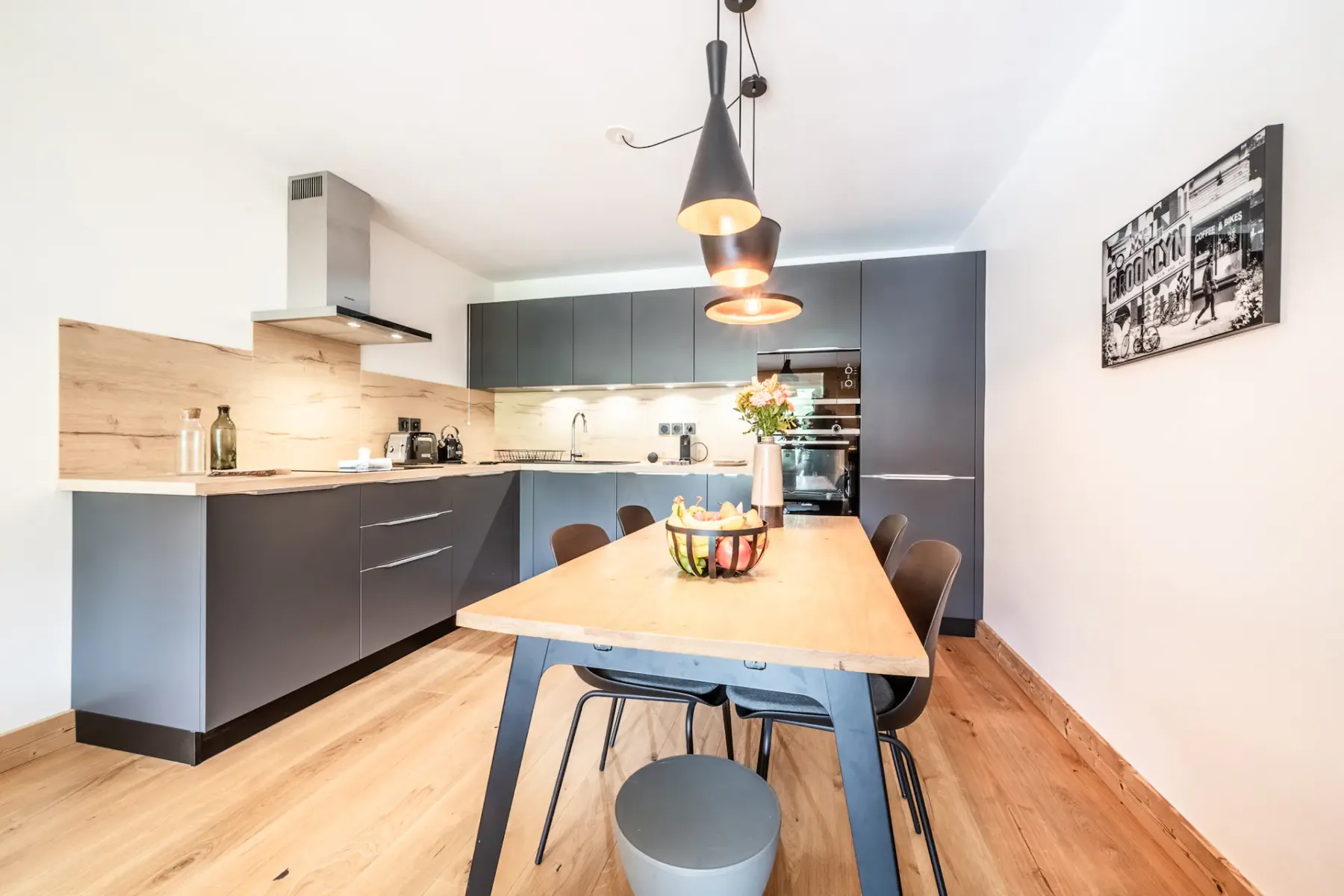 Modern kitchen and dining area with dark cabinets, a wooden table, and pendant lights.
