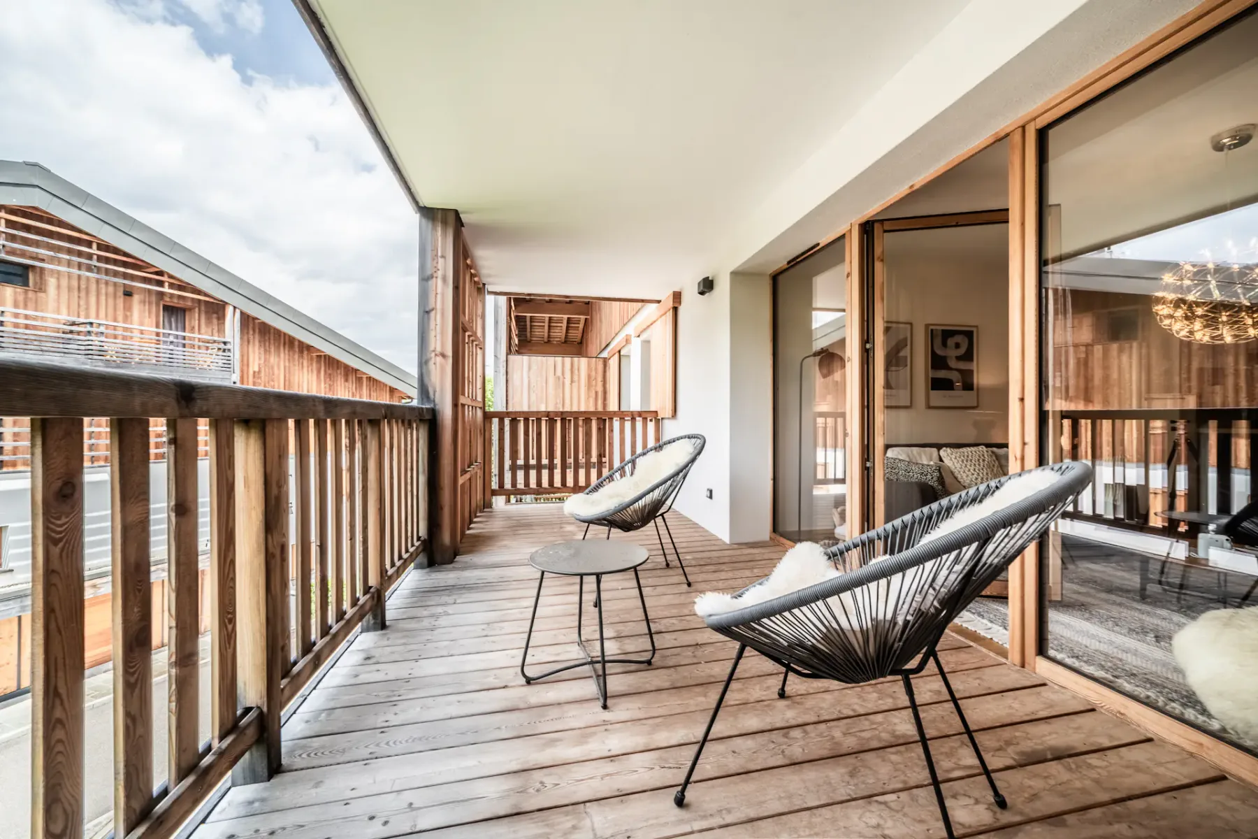 A cozy wooden terrace with a modern chair and table, overlooking green hills, framed by open sliding doors.