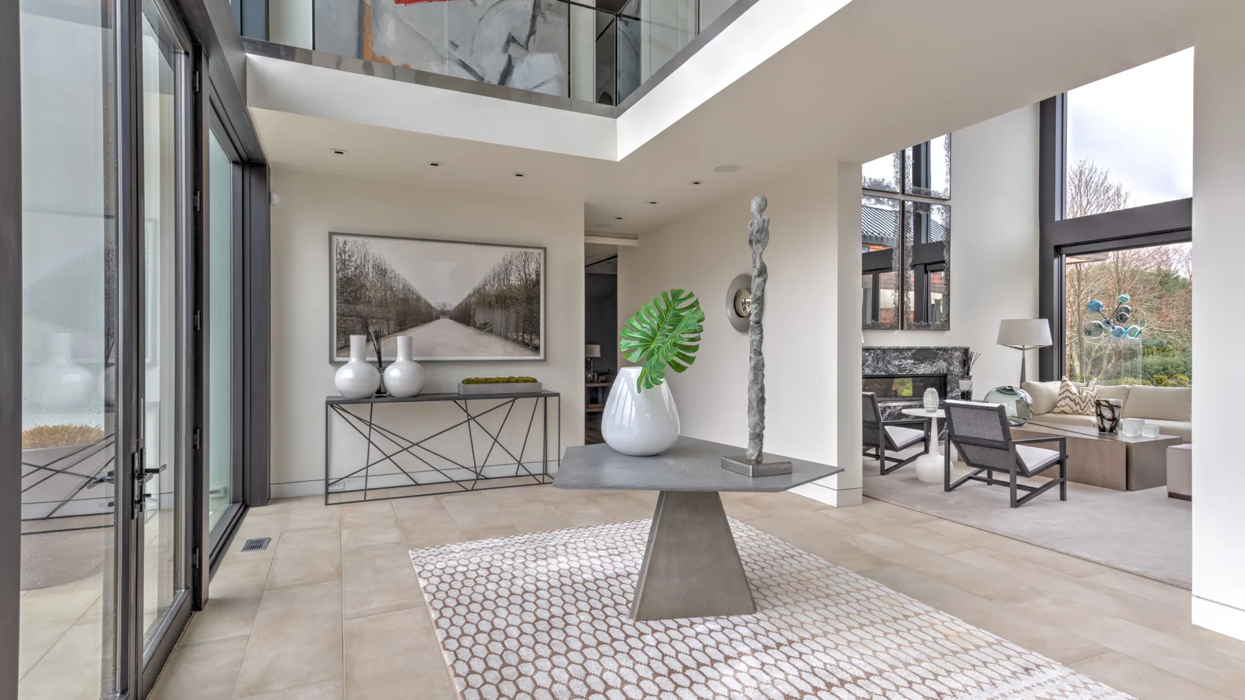 A bright modern interior with a sculptural table and a seating area by tall windows.