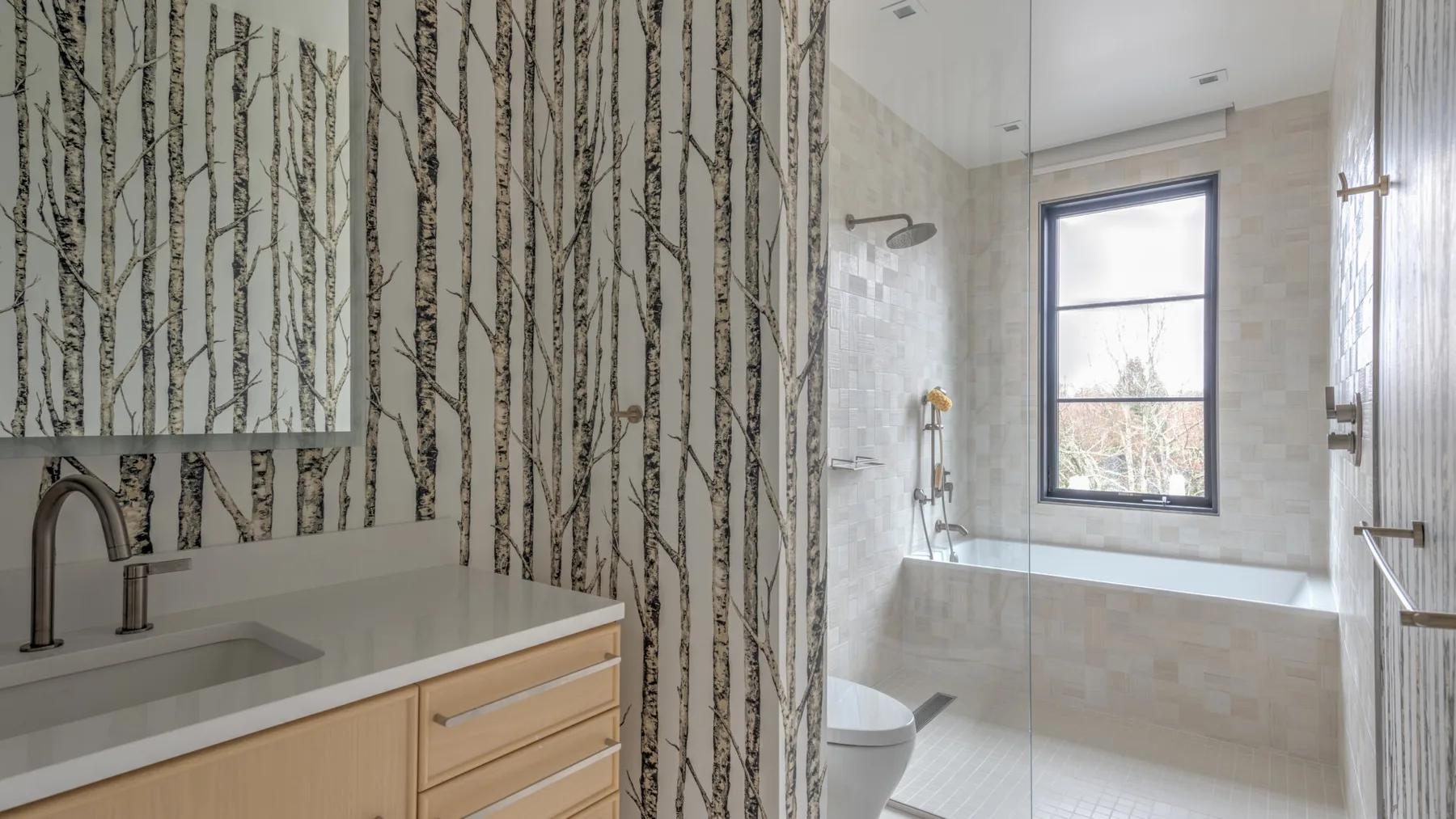 A bathroom with a vanity, shower, and bathtub beneath a window.
