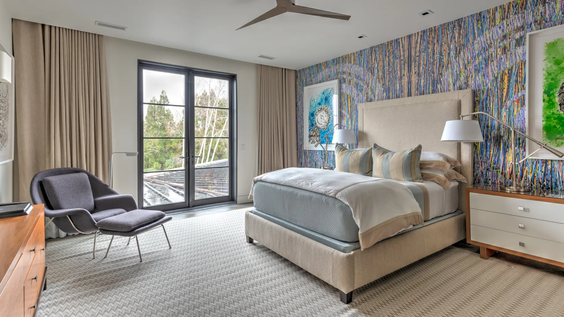 A bedroom with a large bed, colorful patterned wall, and glass doors opening to a balcony.