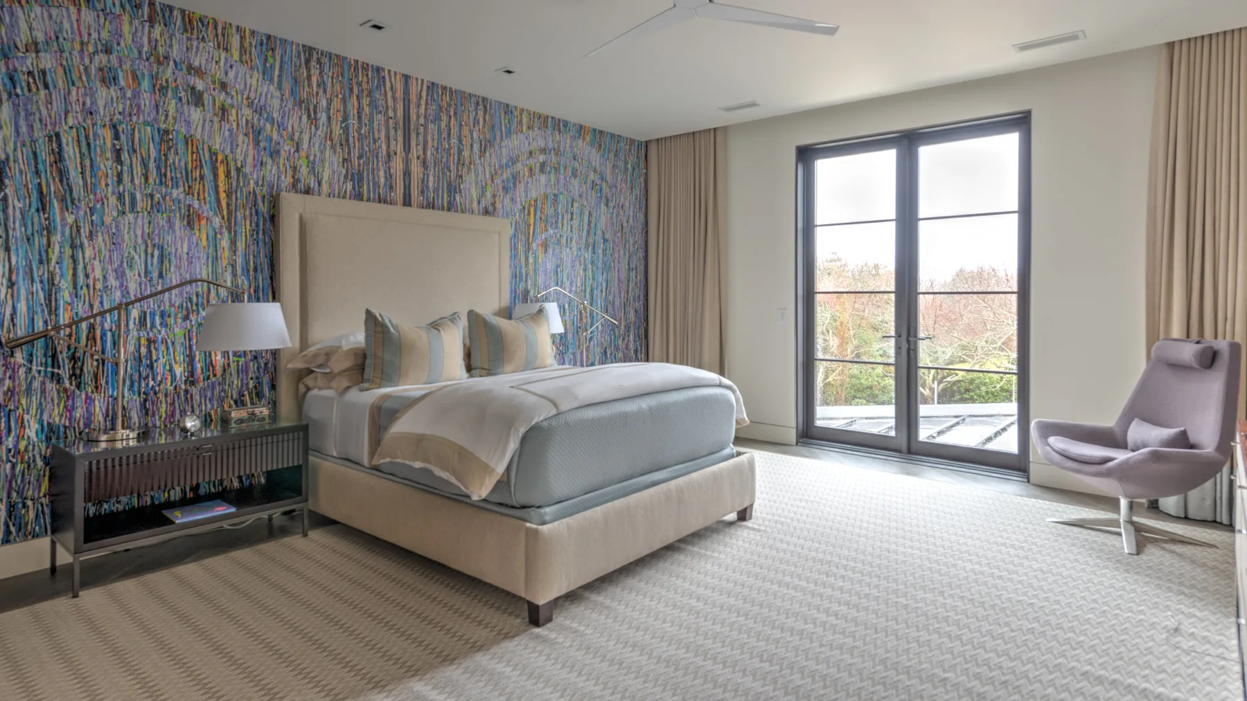 A bedroom with a bed, colorful patterned wall, and large glass doors.
