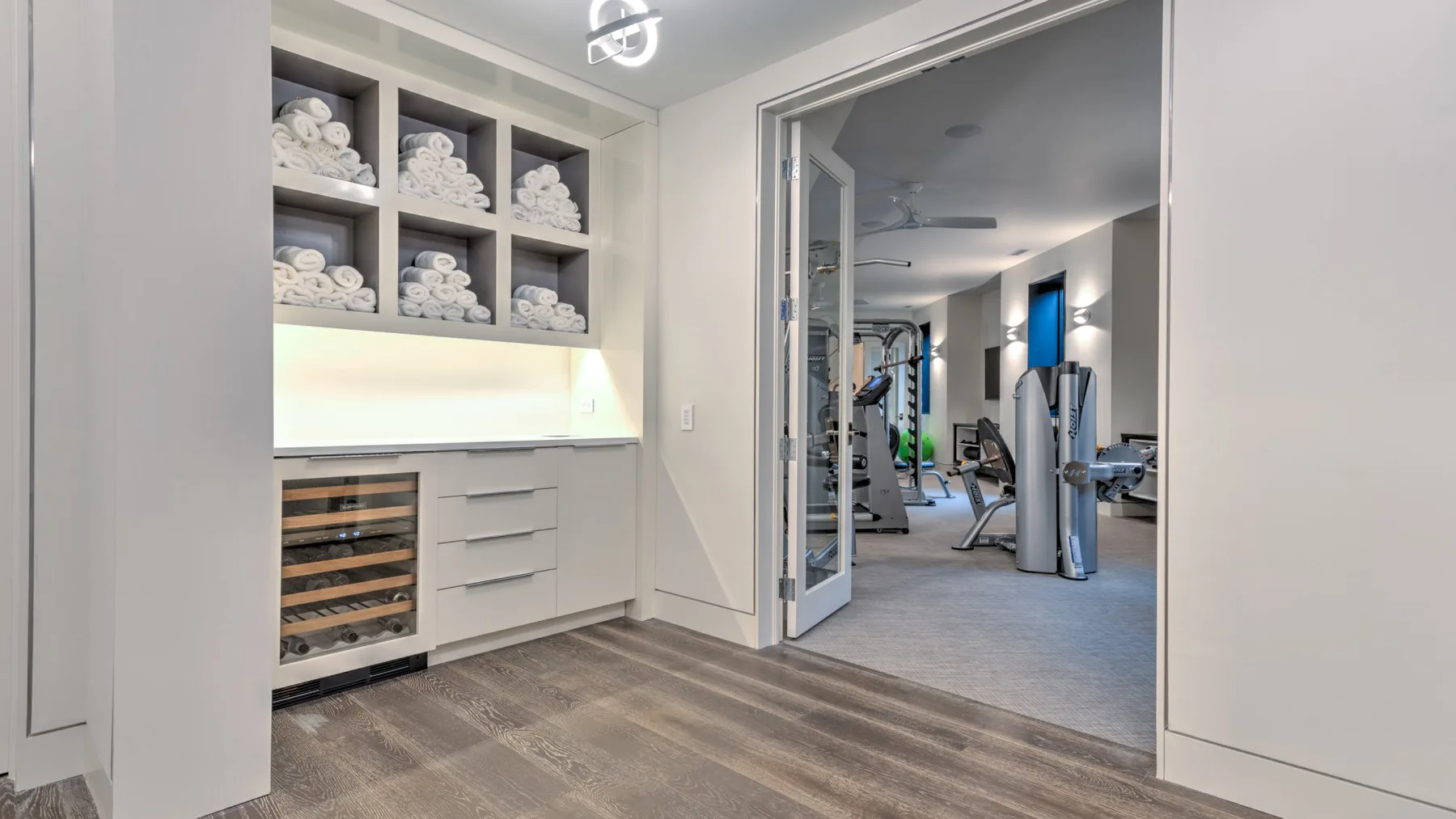 A fitness room is visible through the open doorway beside a towel storage area.
