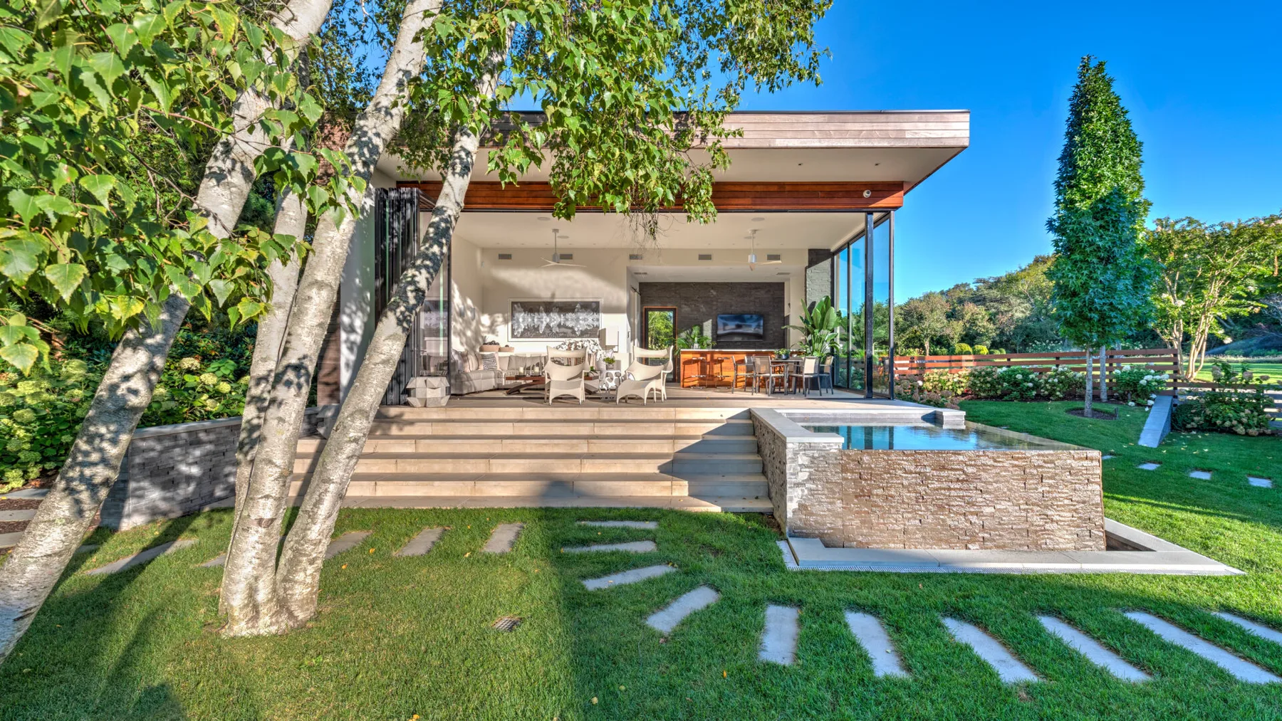 A modern house opens onto a patio, with a rectangular pool and lawn.