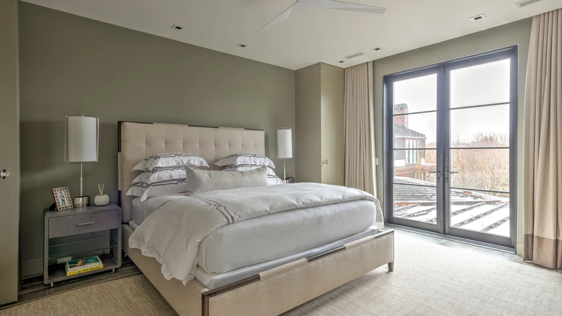 A bedroom with a large bed beside tall windows and curtains.