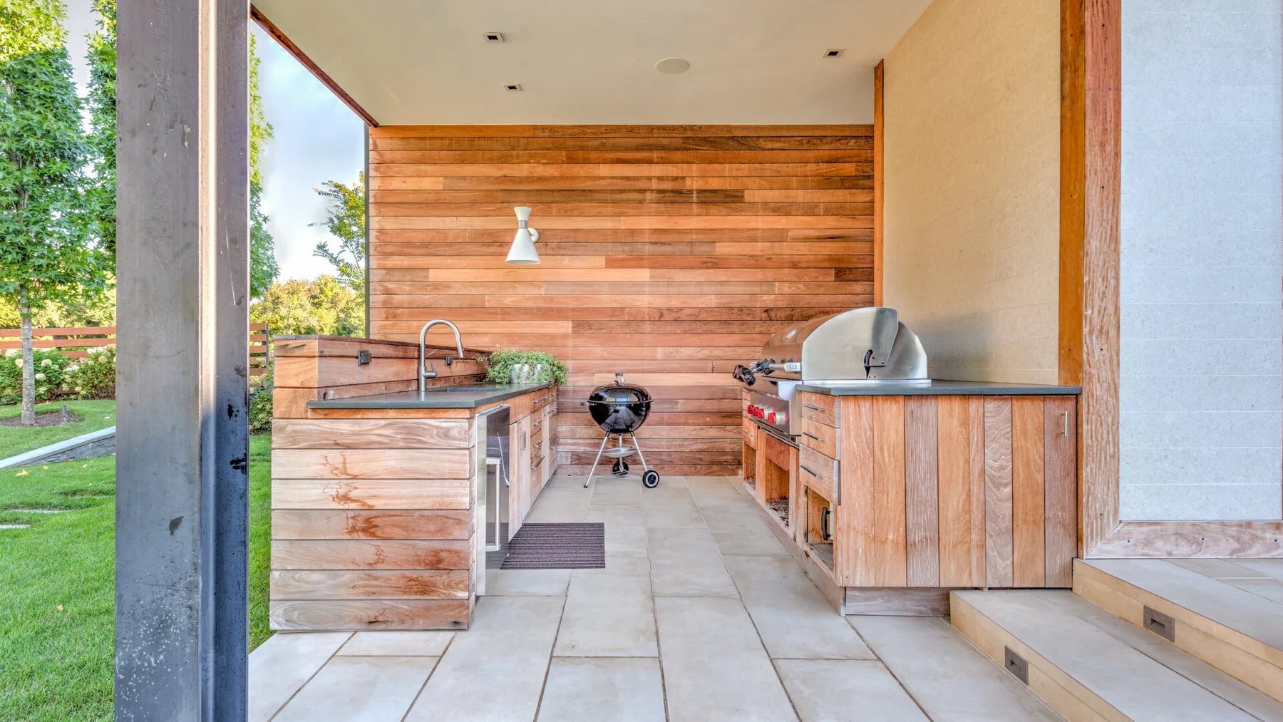 An outdoor kitchen with wooden counters, a grill, and a view of the garden.