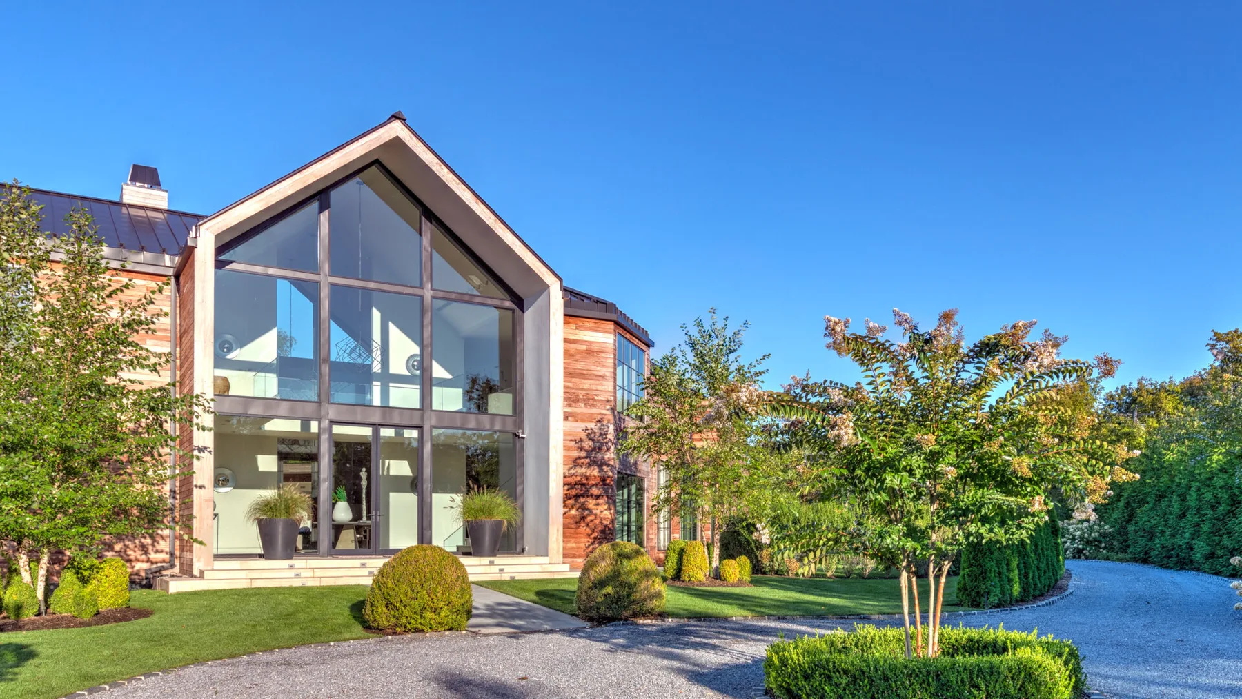 A modern house with a tall glass entrance stands beside a landscaped garden.