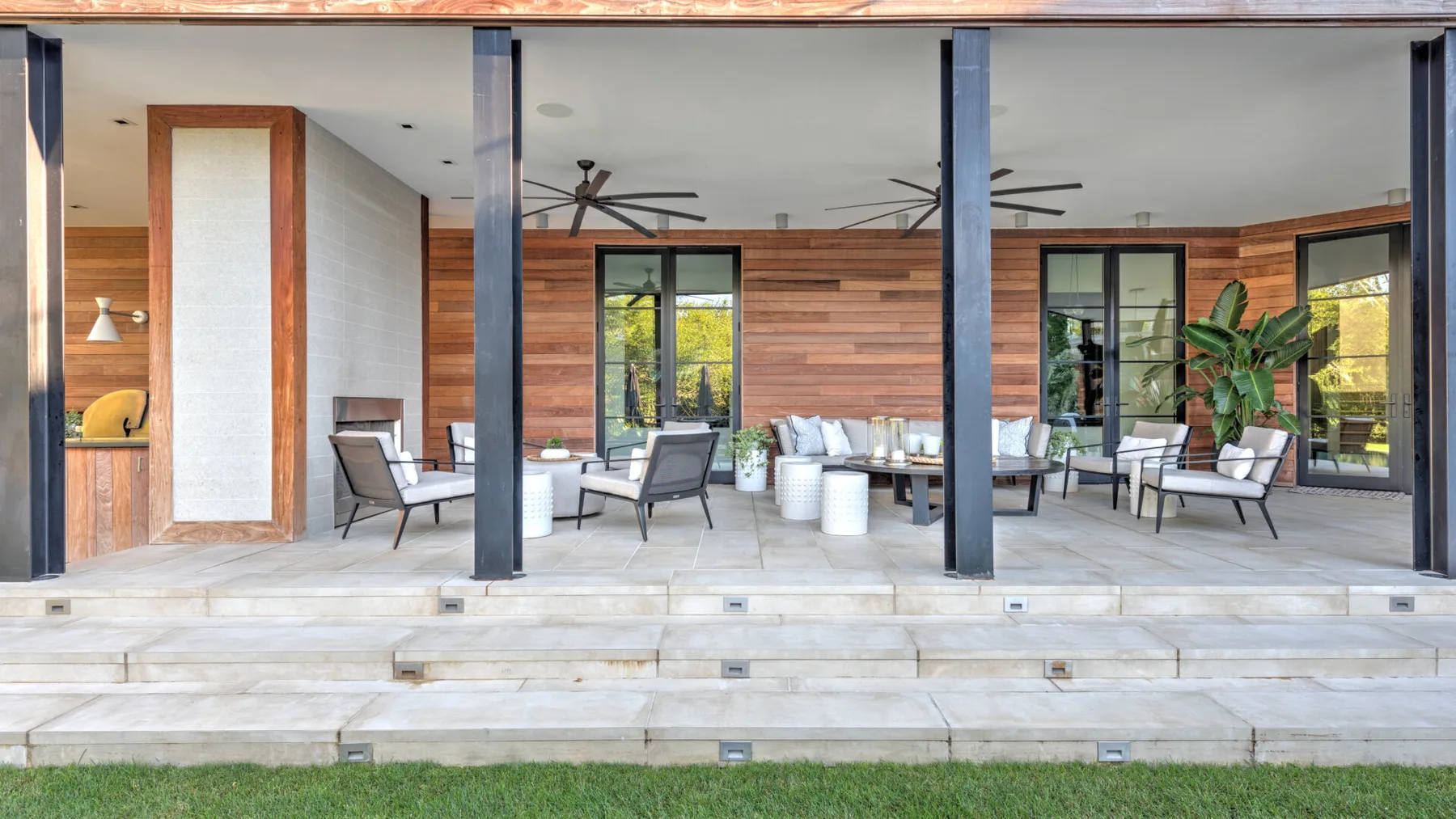 A covered outdoor lounge with seating, ceiling fans, and wooden walls.